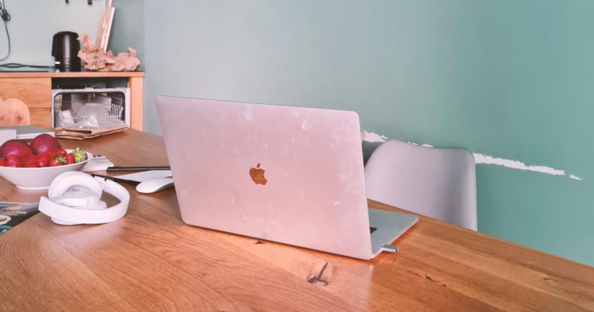 Laptop auf einem Tisch, daneben eine Schale mit Äpfeln und Kopfhörer
